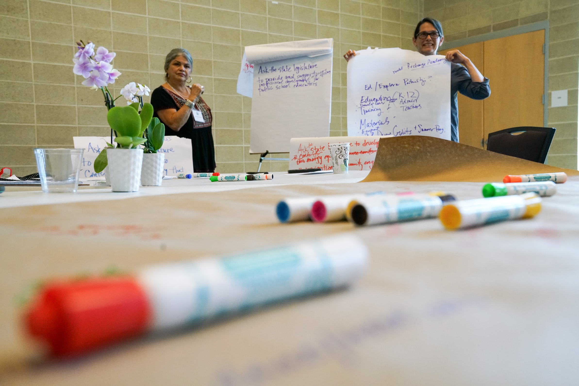 Two women standing by a large paper taking notes and holding up notes